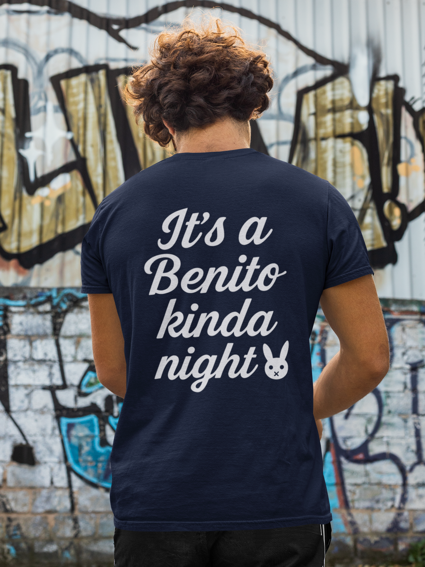 Person wearing a navy blue t-shirt with text in front of a graffiti-covered wall.